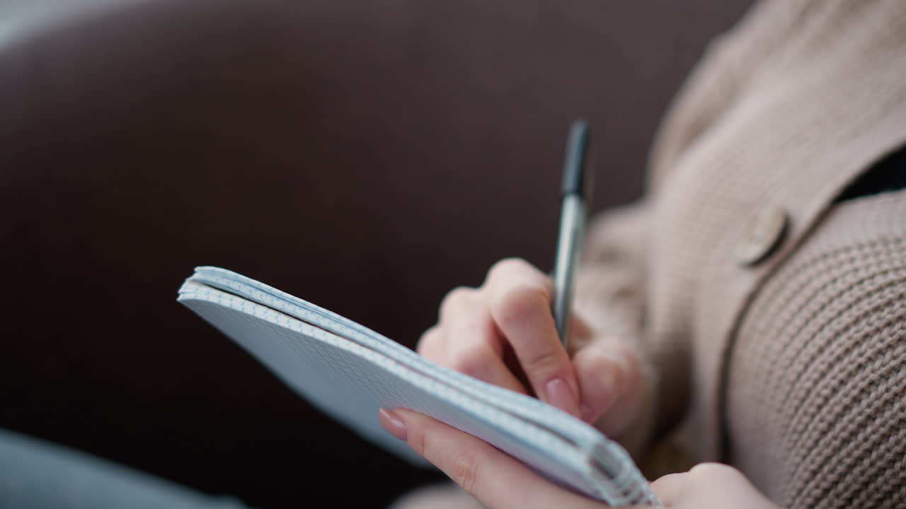 Close-up of hand taking notes in a notebook while wearing a cozy knitted sweater, the soft-focus background creates a warm and focused atmosphere, ideal for studying, journaling, or planning