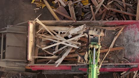 vista de arriba hacia abajo de una máquina industrial cargando escombros de madera en una trituradora de madera, capturando el proceso dinámico de reciclaje y manipulación de materiales en un entorno de sitio de trabajo accidentado.
