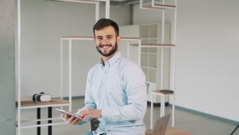 a man in a shirt with a tablet in his hands is looking at the camera and smiling with a caucasian appearance