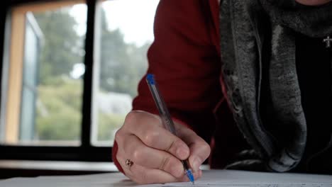 a woman's hand holding a blue ballpen writing inside a cabin in the woods - closeup shot