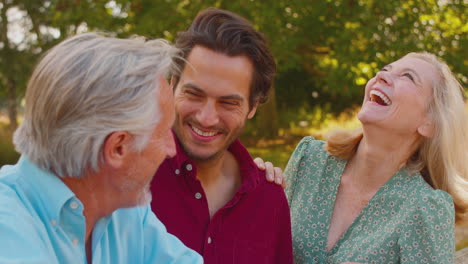 smiling family with mature parents and adult son on walk in summer countryside