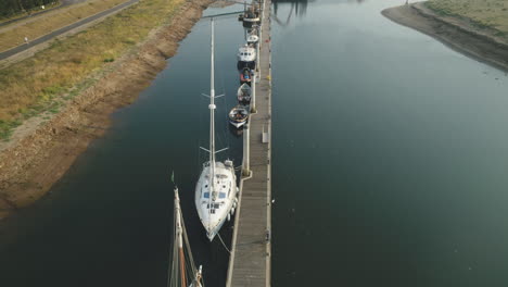 down the line drone shot along small pier with sailing boats and leisure boats in north norfolk