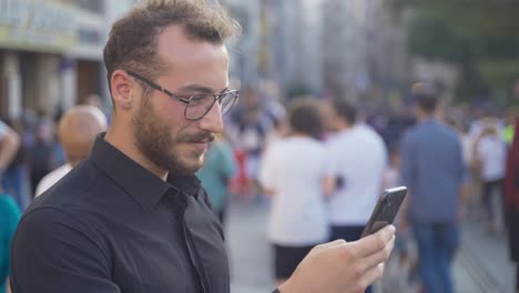 Junger-Mann,-Der-In-Einer-überfüllten-Straße-Eine-SMS-Am-Telefon-Schreibt.