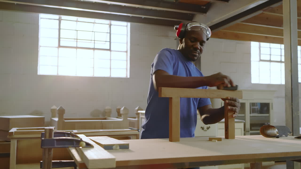 African American man sanding T-shaped frame after coworker pointing rough spot in bright workshop