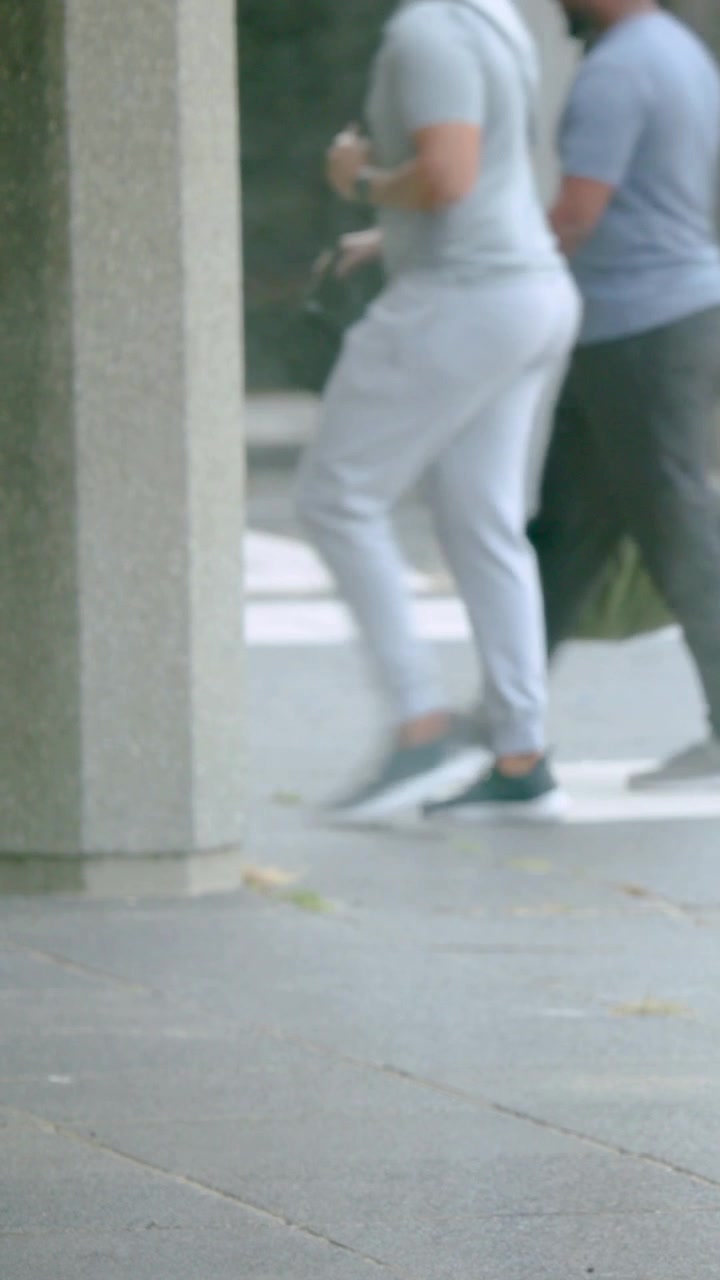 Vertical video: Opening walkway shot showing braided woman in burgundy coat moving, jogger passing