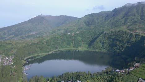 Green-water-lake-surrounded-by-green-trees-of-forest-and-mountain-range