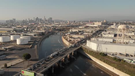 Industriegebiet-Entlang-Des-Laufs-Des-Flusses-La-Mit-Der-Stadt-Los-Angeles-Im-Hintergrund-Und-Dramatischen-Bergen,-Die-Teilweise-Von-Wolken-Bedeckt-Sind