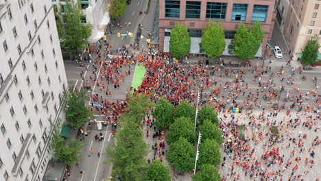 a-Circle-of-People-in-Orange-Shirts-March-on-City-Streets-for-Social-Justice,-Orbiting-Aerial-View