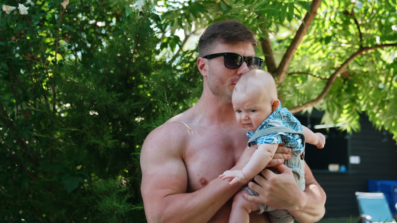 Happy dad holding his infant outdoors. Little infant wants to cry and father tries to calm him down.