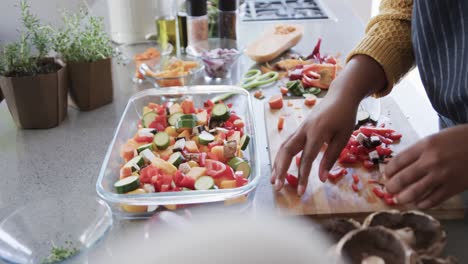 midsection of african american woman in apron preparing meal in kitchen, slow motion