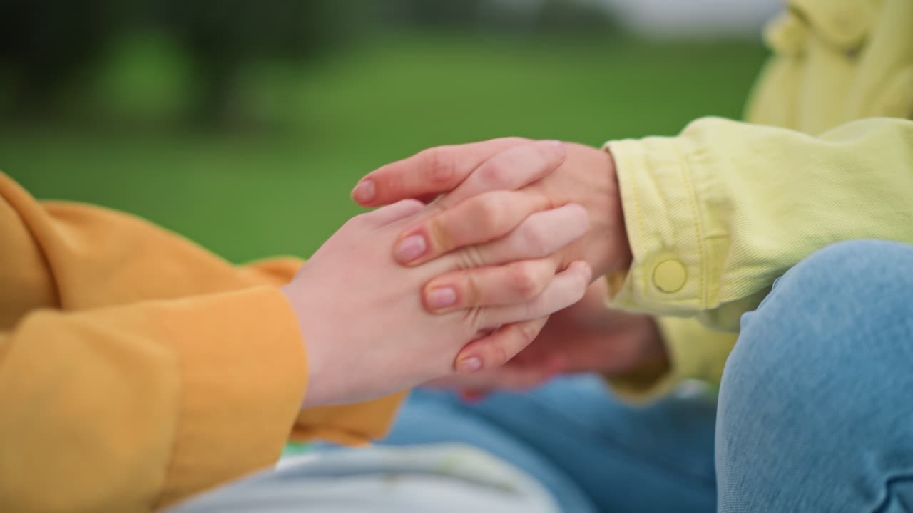 Mujer adulta sosteniendo las manos de un adolescente al aire libre en un parque, con una sonrisa cálida y reconfortante y un suave apretón de manos, contacto cercano y delicado durante una conversación en un picnic, momento de apoyo y fomento de la confianza, natural