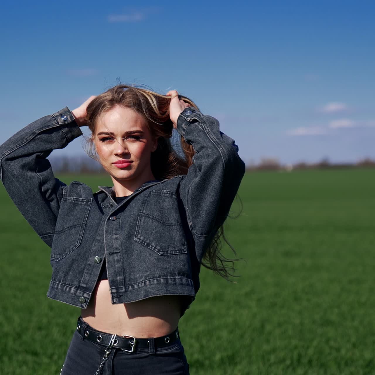 Beautiful girl on field at sunlight. Young woman in denim suit standing with closed eyes to the sun. Attractive model outdoors