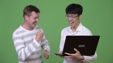 two happy young multi-ethnic businessmen using laptop while getting good news together