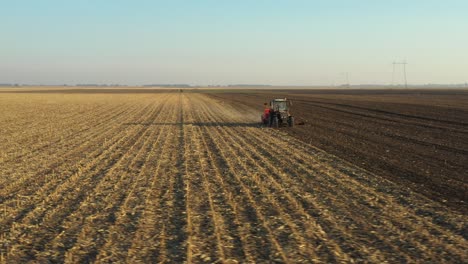 dolly orbit move in aerial top view of tractor as dragging a sowing machine over agricultural field, farmland
