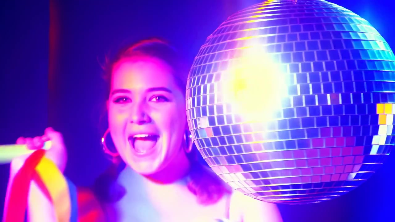 Celebración disco de neón con una mujer joven soplando una corneta de fiesta y agitando serpentinas de colores junto a un brillo