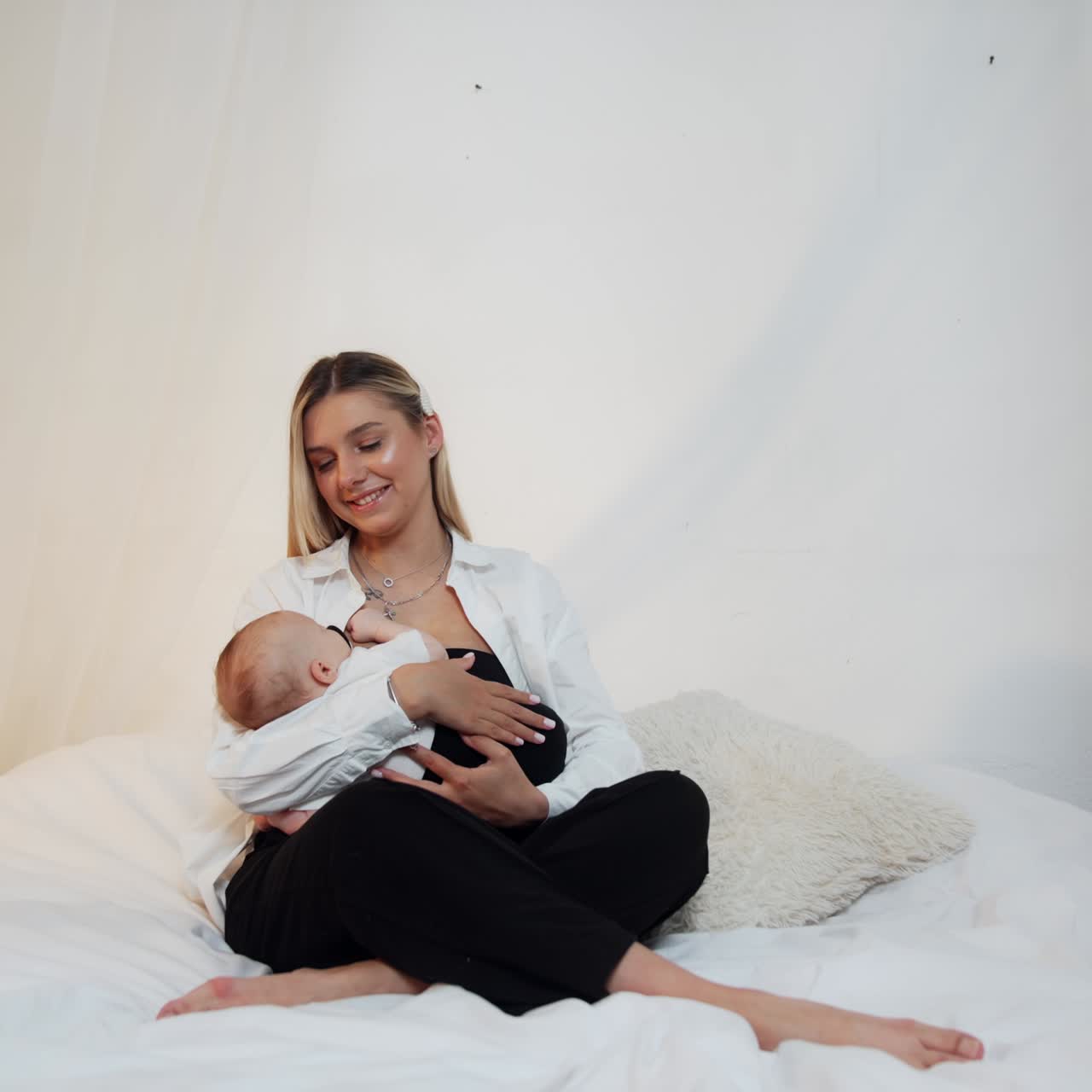 Laughing blonde woman sits on the bed holding a baby in her arms. Mother and child portrait
