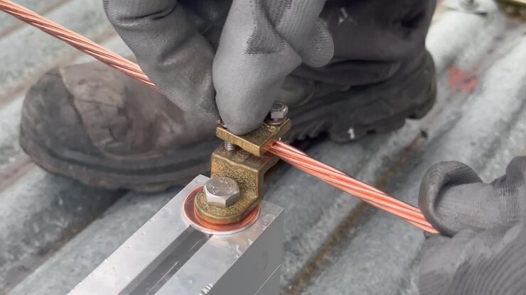 Close-up of a worker's hands manually attaching a grounding braid to an aluminum rail supporting a photovoltaic panel