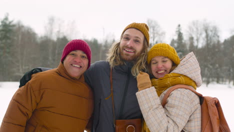 front view of three friends in winter clothes smiling at camera in winter forest