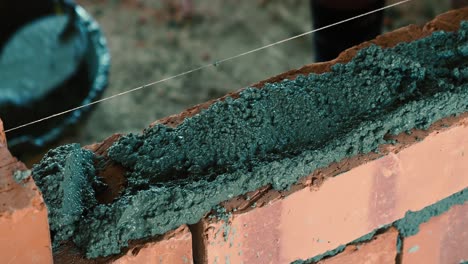 hombre asiático extendiendo mortero y poniendo ladrillos para construir una pared
