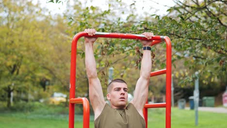 Sportlicher-Junger-Mann-Macht-Klimmzüge-An-Einem-Sportgerät-Im-öffentlichen-Park,-Kamerafahrt