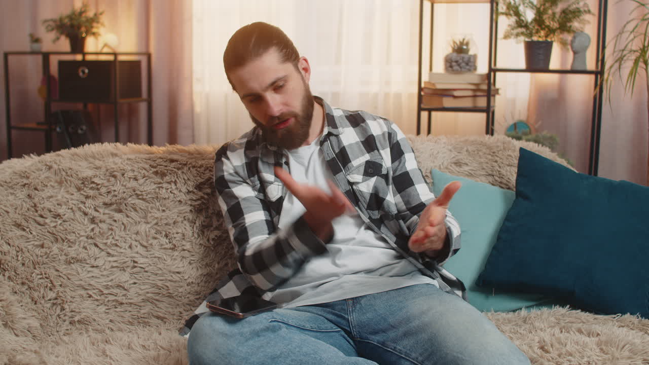 Young man anxious at home urgent phone call on knee frustration loud speaker intense quarrel