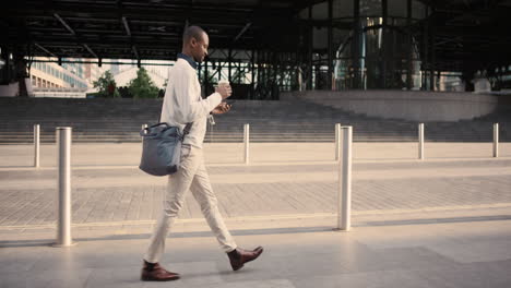 african american businessman walking through city using smart phone