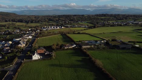 aerial view panning across small town welsh community farmland countryside with snowdonia mountain range on the horizon