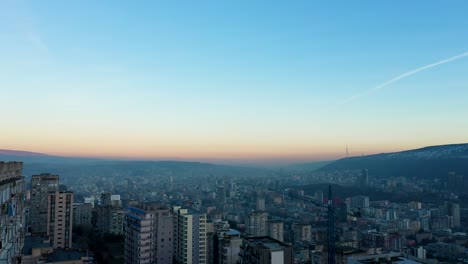 hombre fumando en la azotea con vistas al paisaje urbano de tbilisi en georgia con estela en el cielo al amanecer, drone aéreo