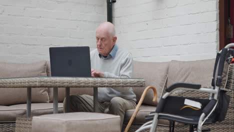 elderly man using laptop with wheelchair nearby
