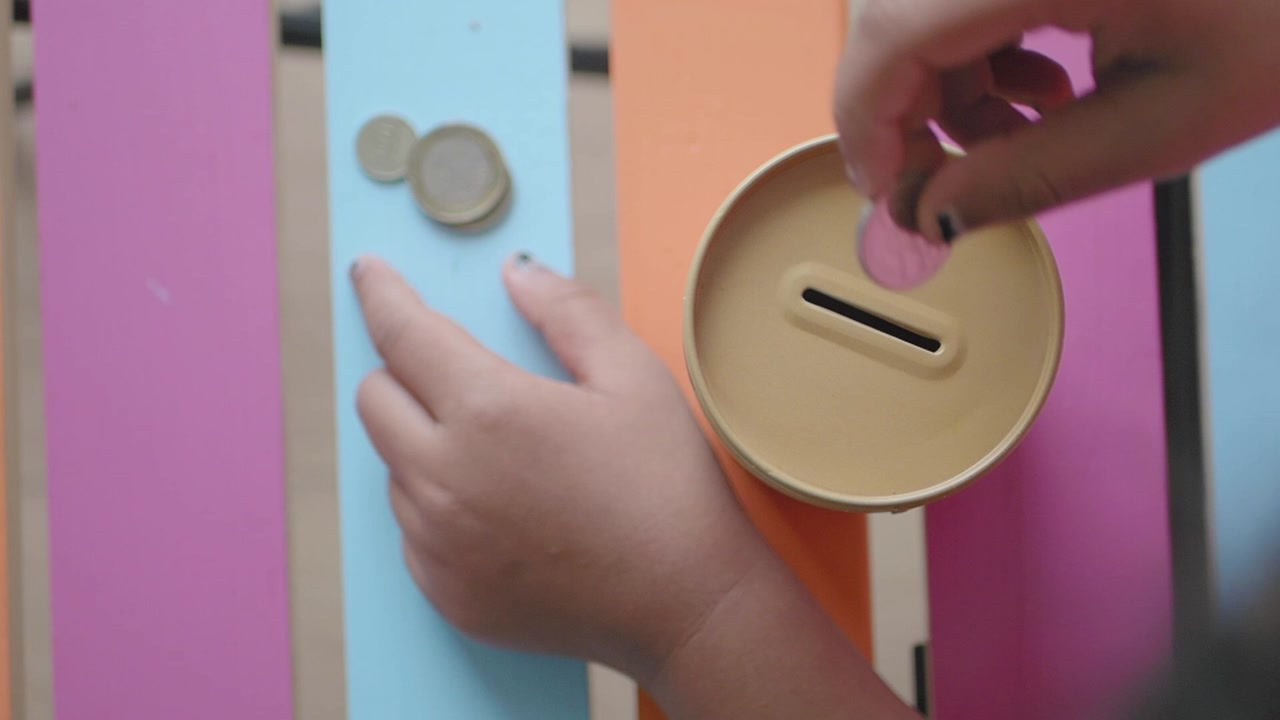 Child's Hands Saving Coins in a Piggy Bank