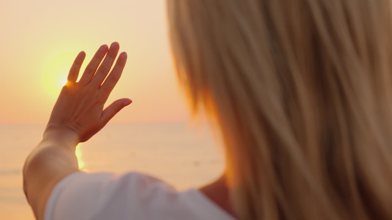 La donna allunga la mano verso il sole che sorge sul mare. Goditi il calore e il volo del concetto