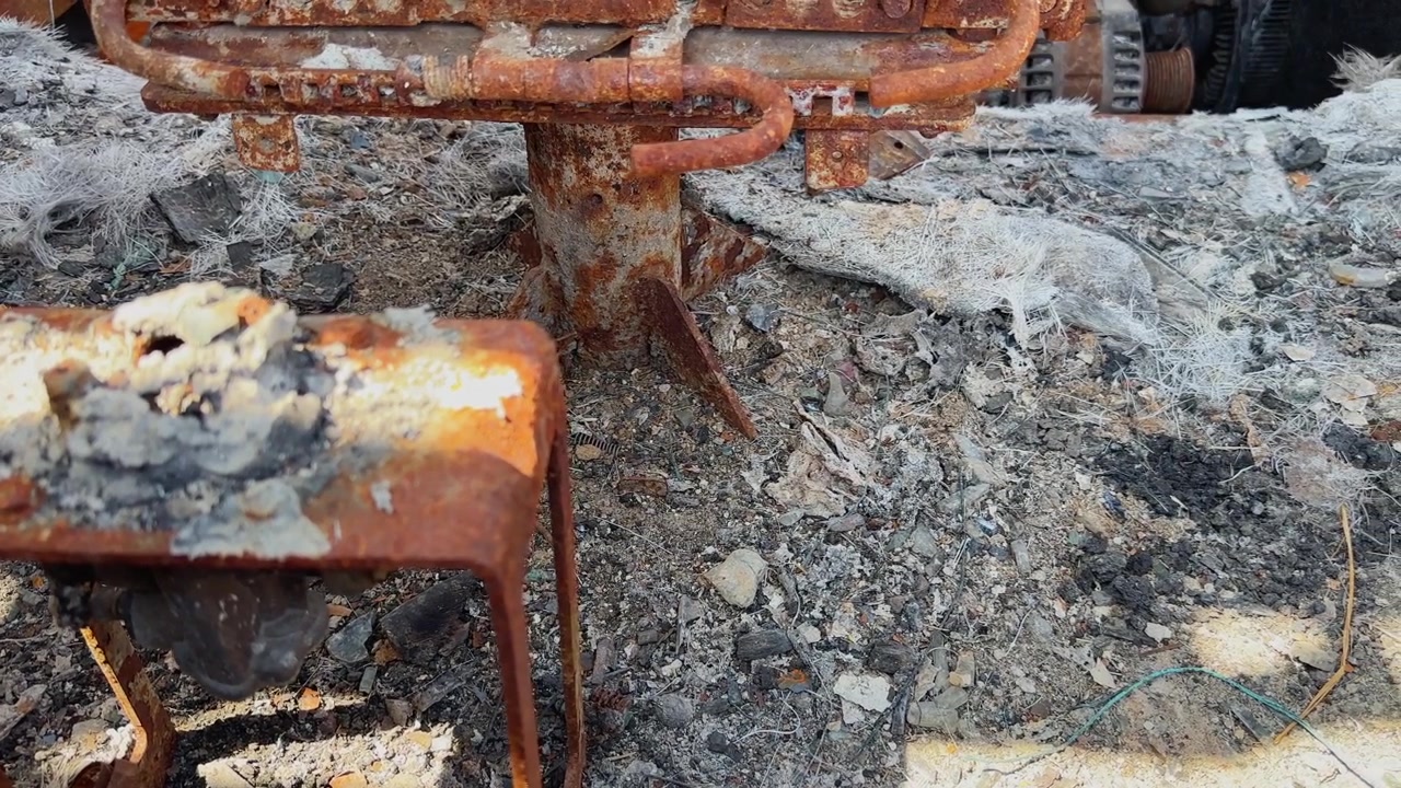 Nærbillede af det brandskadede busgulv dækket af aske, forkullet affald, smeltet glasfiber og rustne metalsædestøtter!