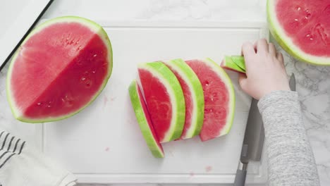 slicing red watermelon into small pieces on a white cutting board.