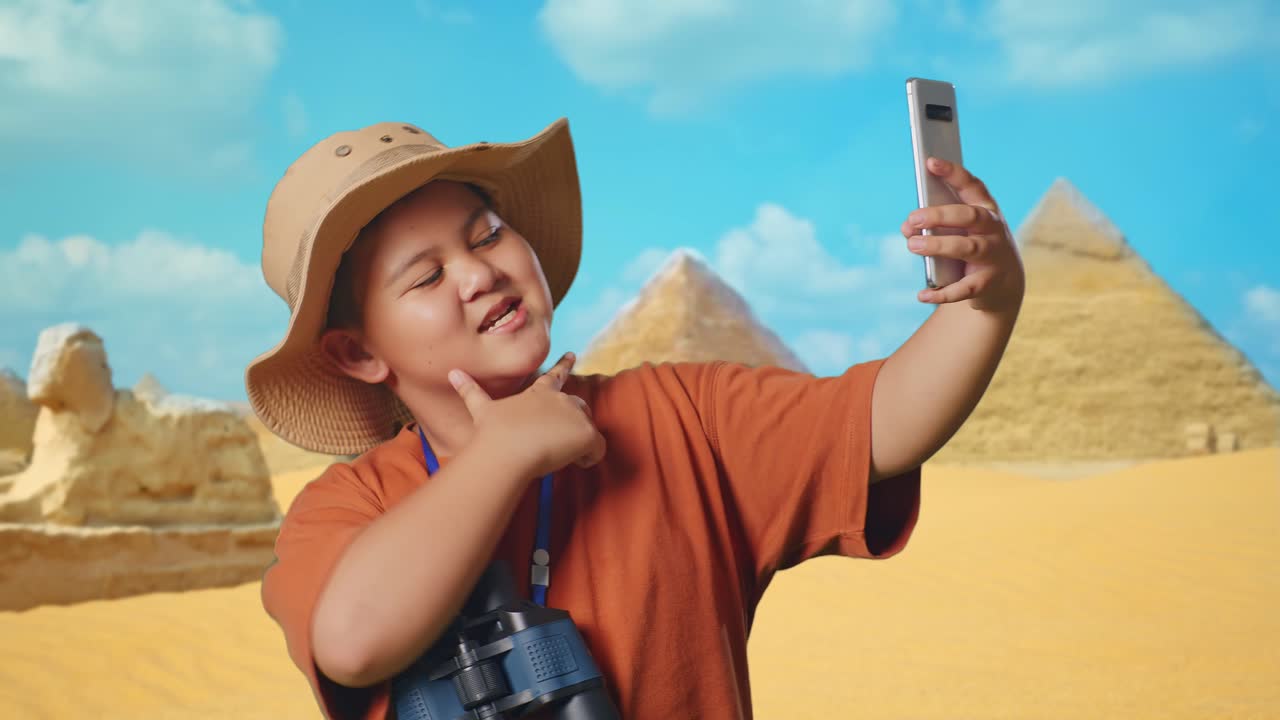 Asian Boy With A Hat And Binoculars Taking A Selfie On Smartphone While Traveling In Giza Pyramid. Boy Researcher Examines Something, Travel Tourism Adventure, Close Up