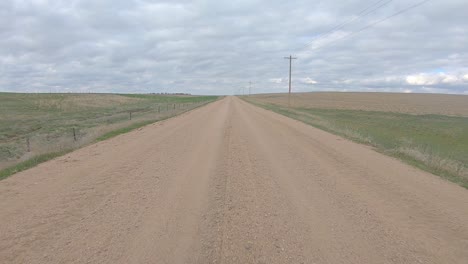 point of view while driving on a straight stretch of gravel road thru rural nebraska on a cloudy day in early spring