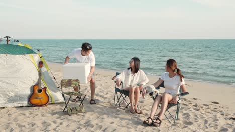 캠프에서 술을 마시고 함께 웃는 친구들, 모래 해변에서 휴가를 즐기는 친구들, 캠핑 텐트 근처, 해가 지면 휴가 시간.