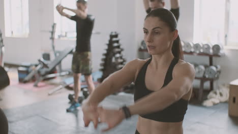 a strong and athletic young woman does arms and shoulders stretching exercises in the gym