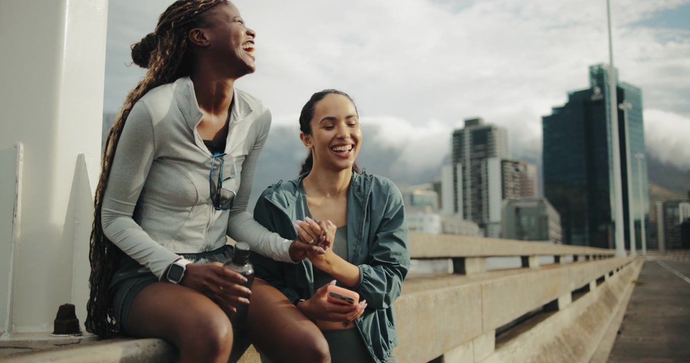 Two Young Women Resting and Using Smartphone on City Bridge
