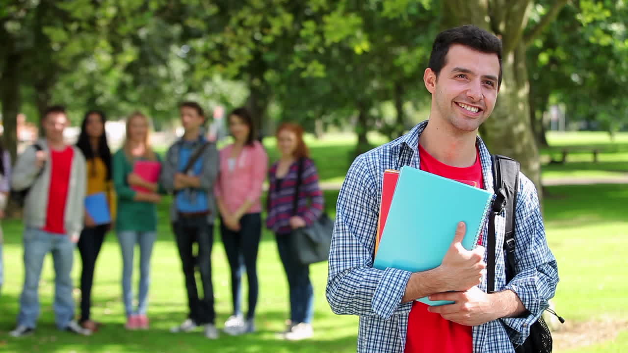 estudiante sonriendo a la cámara con amigos de pie detrás de él en la hierba