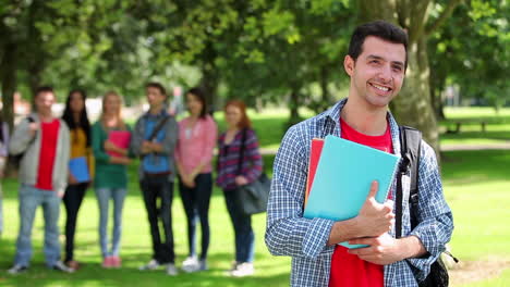 student smiling at camera with friends standing behind him on grass