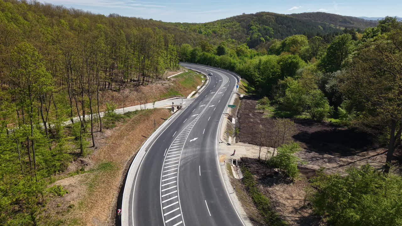 Una vista aerea mostra una moderna autostrada asfaltata che si snoda attraverso una fitta foresta verde su dolci colline durante la primavera.