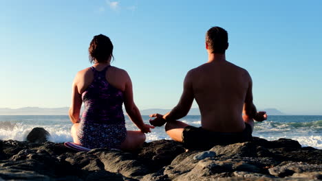 couple meditate at sunrise on coastal rocks after swim facing crashing waves