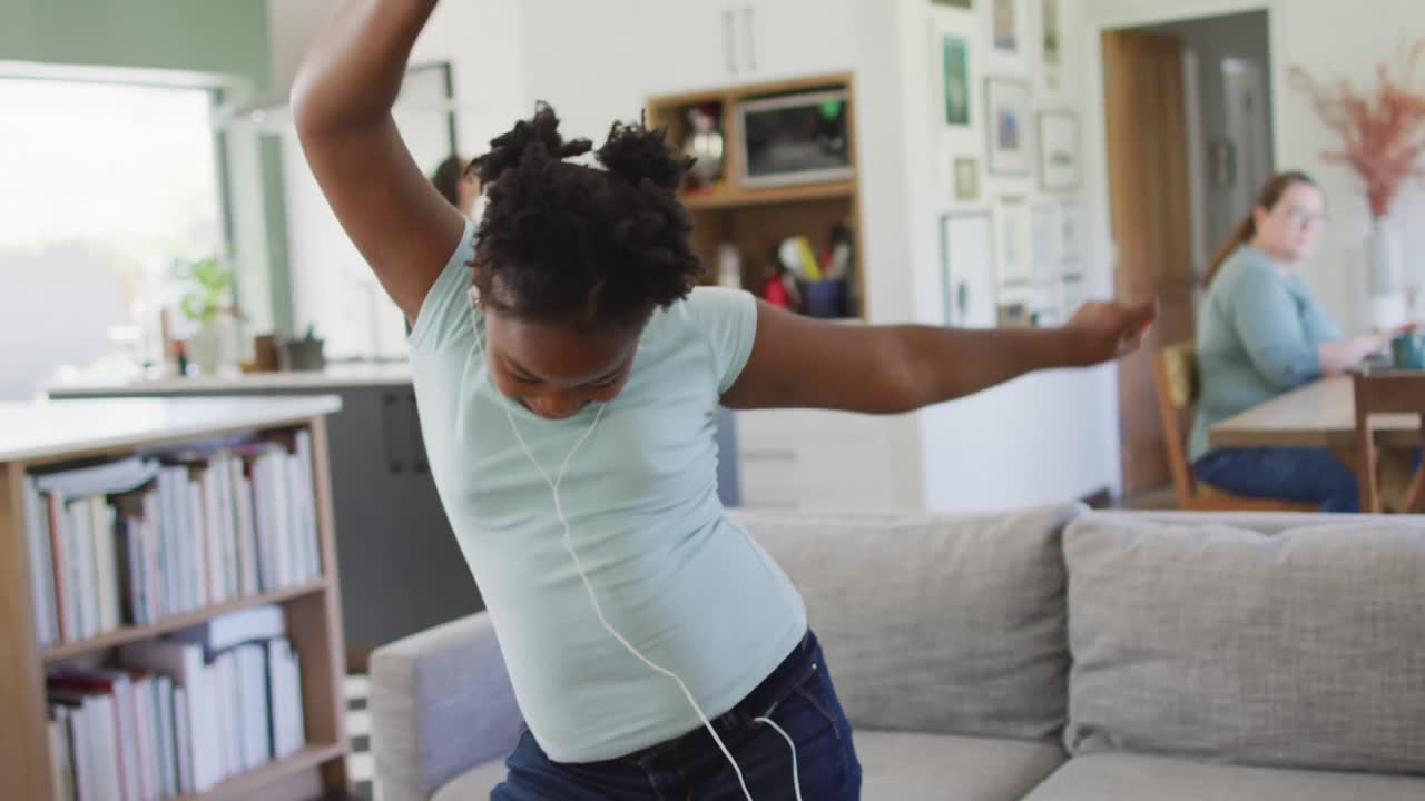 Happy african american girl wearing earphones and dancing in living room