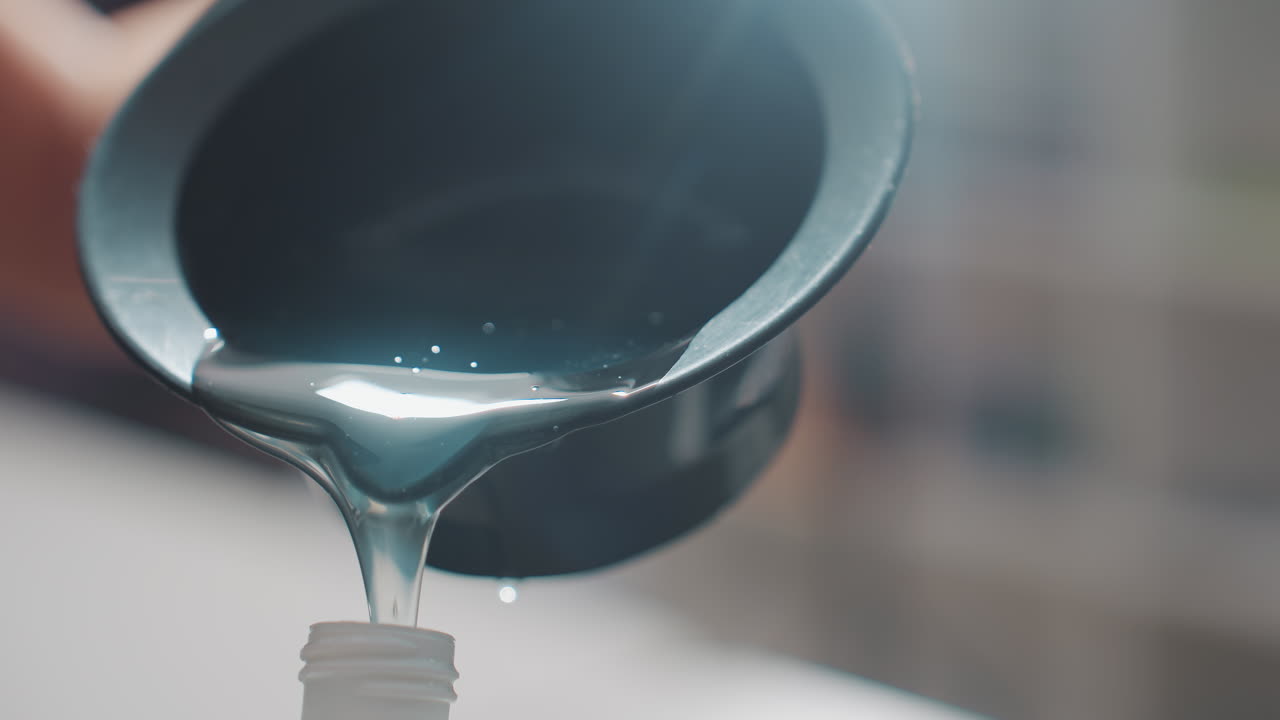 tintura azul brillante cayendo en cascada dentro de una botella, gran flujo por el borde, superficie resplandeciente, puntería precisa y manos firmes, mostrador de salón moderno con suave luz de fondo natural, textura del producto visible