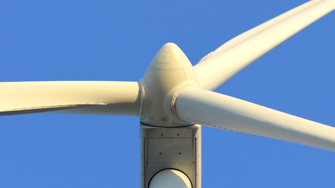 Primo piano di una turbina eolica che gira contro un cielo azzurro limpido. Pale bianche che generano energia rinnovabile e sostenibile in un moderno parco eolico.