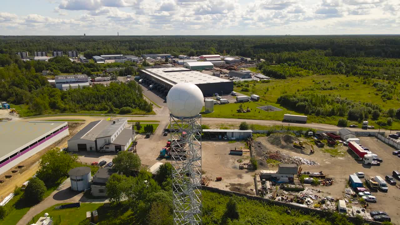Aerial drone footage orbiting and flying around a modern weather observatory radar dome or white colored radome during a sunny summer day with landscape and city in the horizon at the background