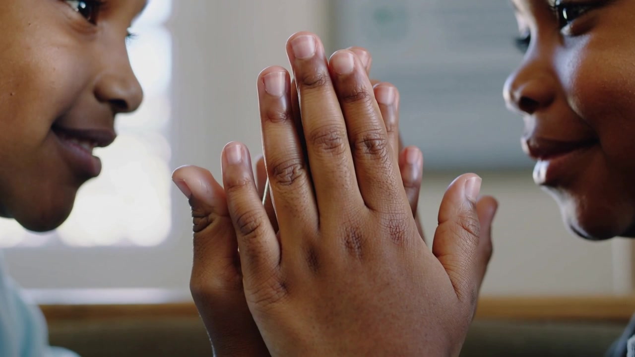 Pressing palms together, two kids playing handclap on bench near window in blue and gray tops