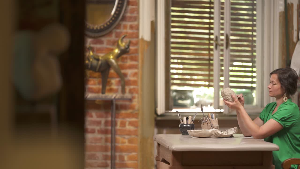 영감을 받은 아름다운 여성이 전문적인 도구를 사용하여 세라 비를 주의 깊게 글래싱하는 측면 전망. 스튜디오에서 일하는 전문 예술가. 배경에 세련된 인테리어 워크.