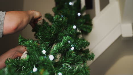 Hands-of-person-attaching-Christmas-decorations-to-a-railing-along-the-stairs-of-their-home-to-decorate-for-the-holiday-season