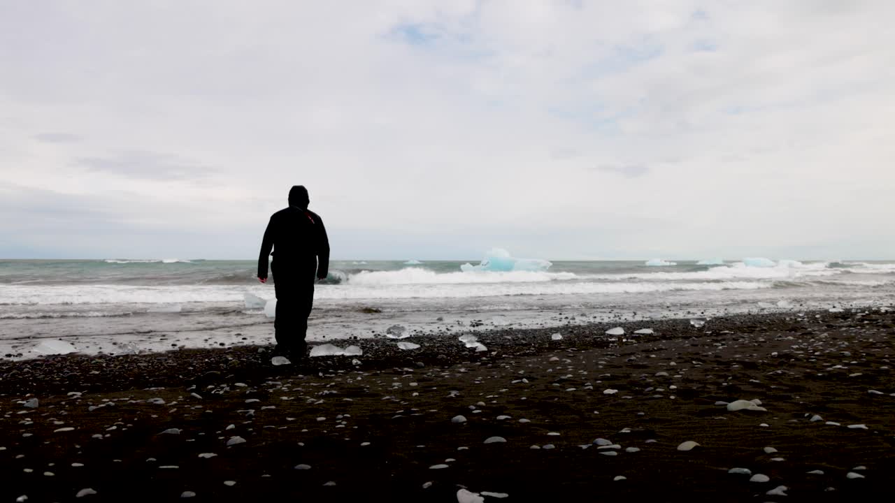 아이슬란드의 빙하 석호에서 검은 모래 해변을 걷는 남자